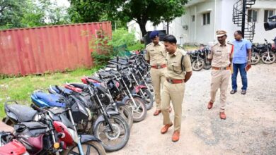 Police officers inspect a long row of recovered stolen motorbikes lined up in a station yard.