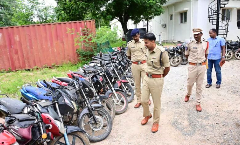 Police officers inspect a long row of recovered stolen motorbikes lined up in a station yard.