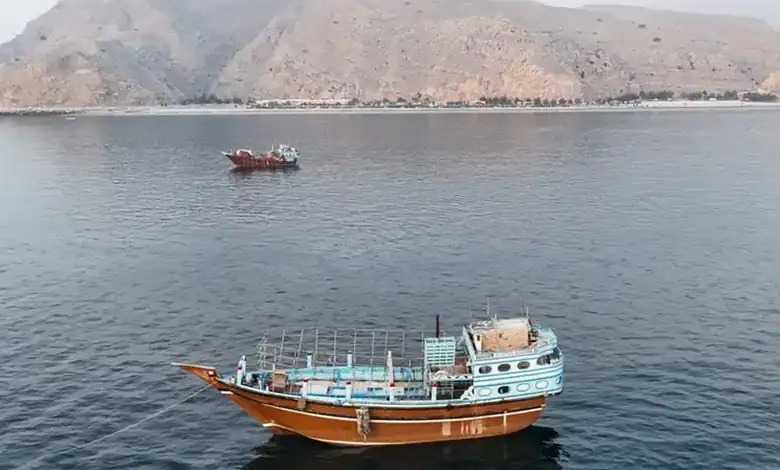 A boat sailing in the Strait of Hormuz with mountainous terrain in the background.