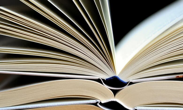 Close-up of an open book with pages fanned out, showing detailed text and a dark background.