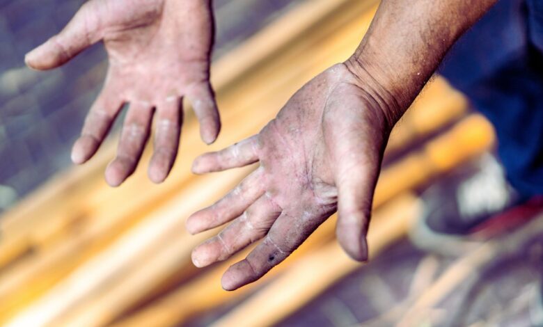 Close-up of two dirt-streaked hands with palms raised, wooden planks blurred in the background.