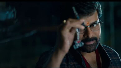 Close-up of a man with glasses and a beard adjusting his glasses in a dark setting.