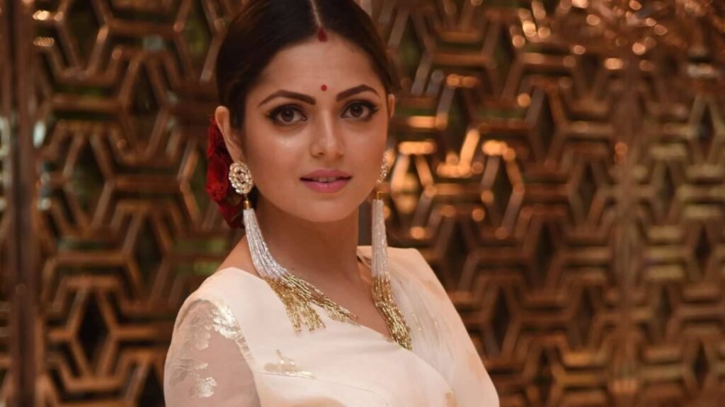 Indian woman wearing traditional saree and jewelry with a decorative background.