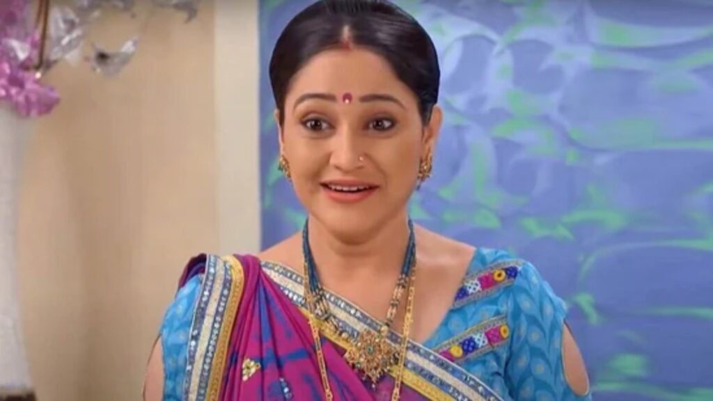Indian woman wearing a blue saree with gold jewelry and a red bindi, smiling.