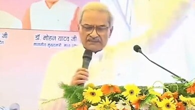 BJP MP speaking at a podium decorated with yellow and orange flowers during a public event.