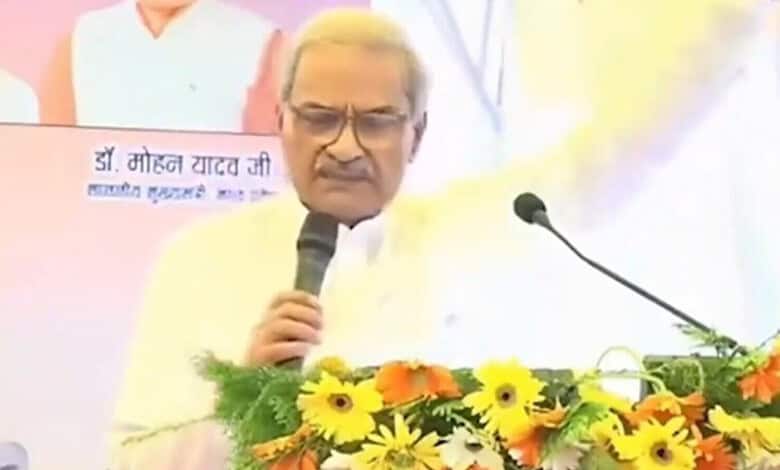 BJP MP speaking at a podium decorated with yellow and orange flowers during a public event.