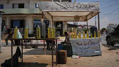 Street vendor selling bottles of cooking oil under a makeshift tent in Gaza.