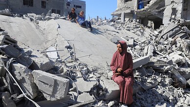 Woman sitting on rubble in Gaza after destruction from conflict.