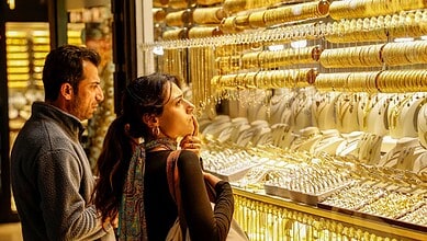 Couple shopping for gold jewelry at a Dubai store with bright display cases.