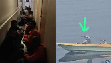 Crew members take cover inside a vessel as a small boat approaches.