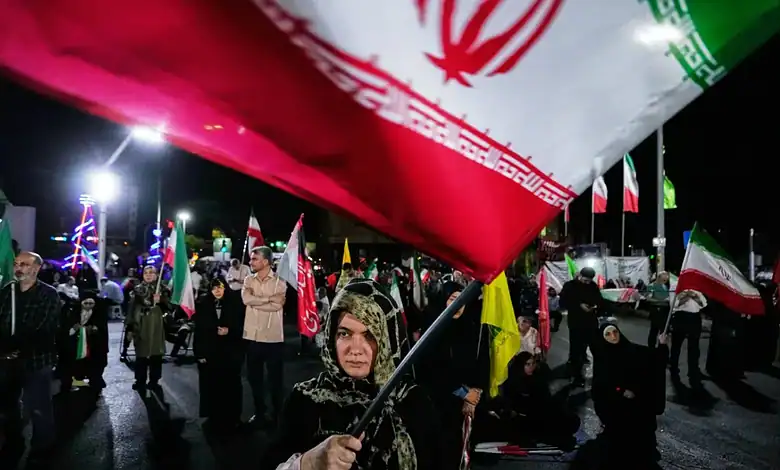 Woman holding Iranian flag during night protest with crowd and flags in the background.