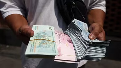 Person holding a large stack of Iranian rial banknotes, indicating currency devaluation.