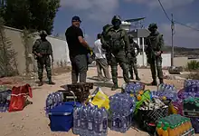 Israeli soldiers and detained individuals near water bottles and supplies in an outdoor setting.