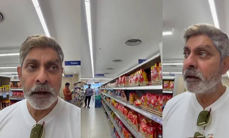 Man with grey hair and beard shopping in a supermarket aisle with snack shelves.