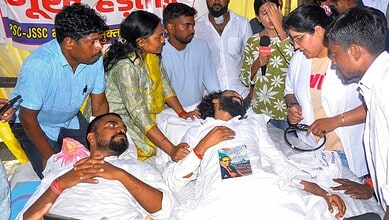 Students and supporters gather around hunger strike patient in hospital bed during protest.
