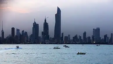 Kuwait City skyline with skyscrapers and boats on the water at dusk.
