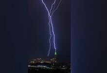 A lightning bolt strikes the illuminated Makkah Clock Tower at night as the city skyline lies below.