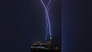 A lightning bolt strikes the illuminated Makkah Clock Tower at night as the city skyline lies below.