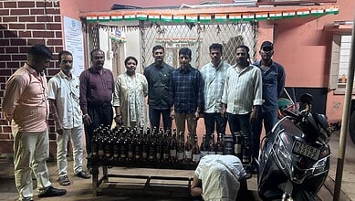 Group of people standing behind a table with bottled drinks and a motorcycle nearby.