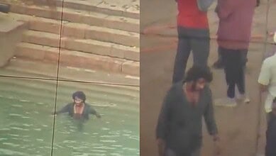 People near a water body with a brick wall in the background, some standing and some in the water.