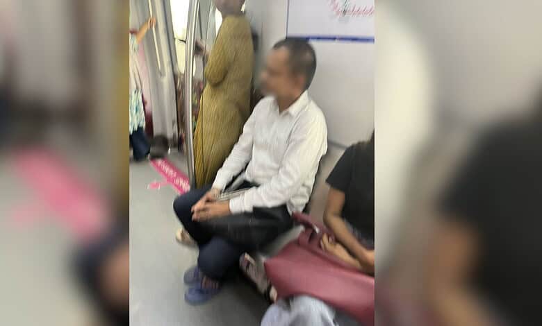 Man sitting in ladies' coach of Hyderabad Metro, surrounded by women passengers.