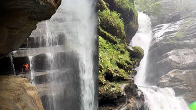 Scenic waterfall with a cave behind it, lush greenery surrounds the area.