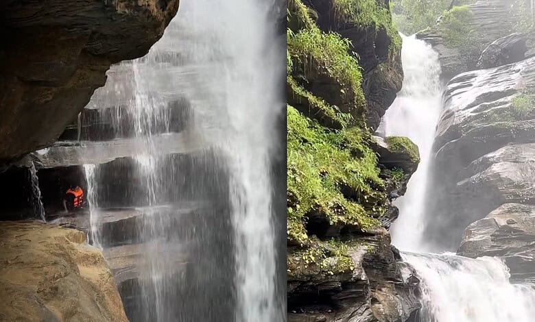 Scenic waterfall with a cave behind it, lush greenery surrounds the area.