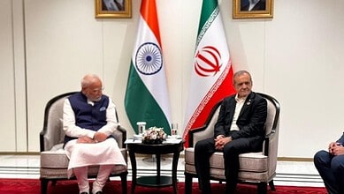 Indian Prime Minister Narendra Modi and Iranian official meet in formal setting with flags behind them.