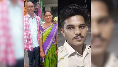Two men and a woman standing outdoors, one in a white shirt and pink scarf, the other in a purple saree.