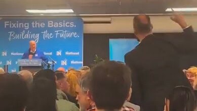 Protester confronts NZ PM Luxon during a political event with a crowd present.