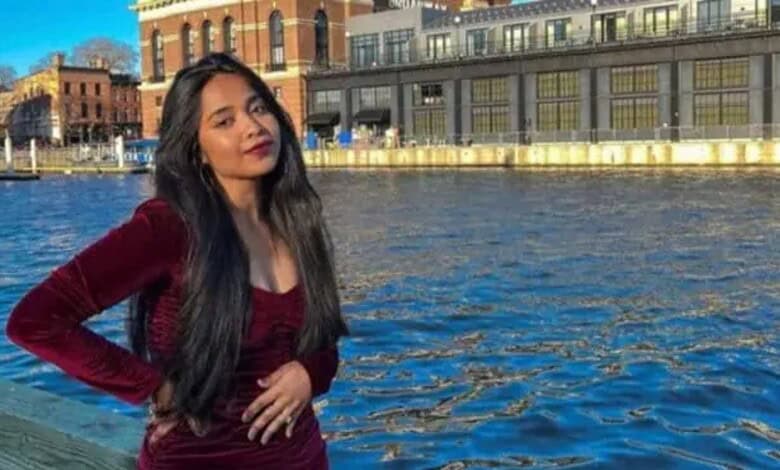 Young woman with long dark hair in a maroon dress by the river in an urban setting.