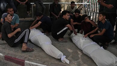 Group of young Palestinians mourning and sitting around two covered bodies in Gaza.