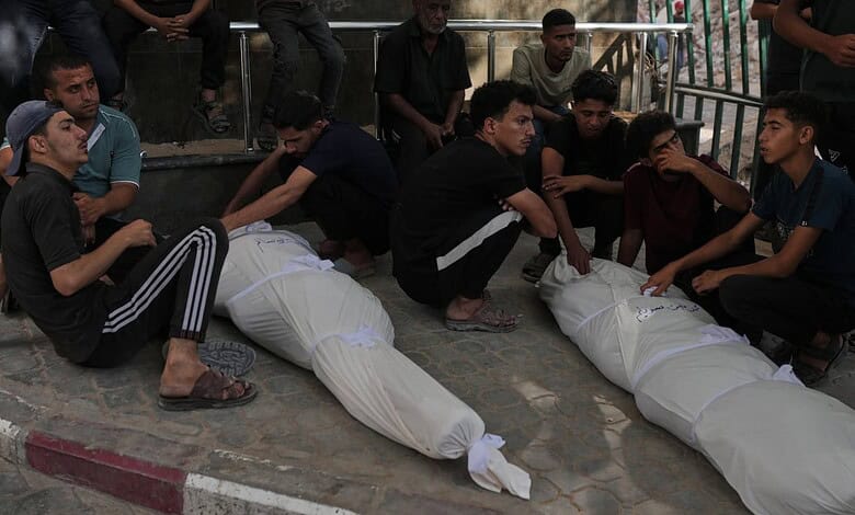 Group of young Palestinians mourning and sitting around two covered bodies in Gaza.