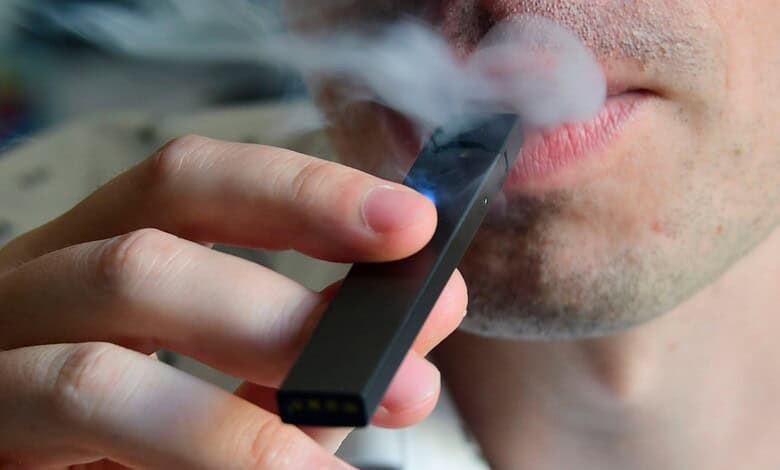 Close-up of person exhaling vapor from an e-cigarette device.