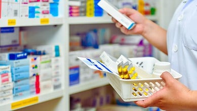 Pharmacist holding a basket of pills and medication in a pharmacy setting.
