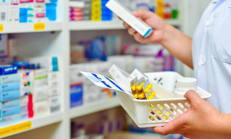 Pharmacist holding a basket of pills and medication in a pharmacy setting.