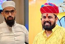 Two men in traditional attire, one with a white cap and the other with a red turban, smiling.