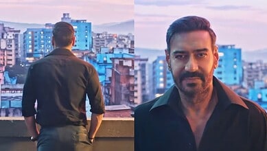 Man with beard in black shirt on rooftop with city skyline at sunset.