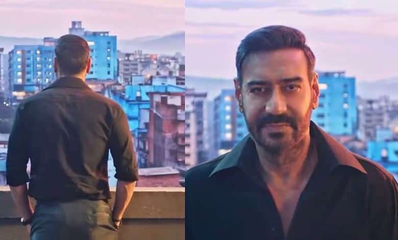 Man with beard in black shirt on rooftop with city skyline at sunset.