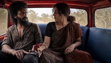 Two people sitting in a vehicle, engaged in conversation, with a rural landscape outside.
