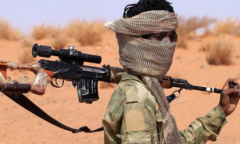 Rebel fighter with rifle in desert landscape, wearing scarf covering face, holding weapon over shoulder.