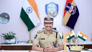 Hyderabad police chief Sajjanar smiling in his office with Indian flags and police emblems behind him.