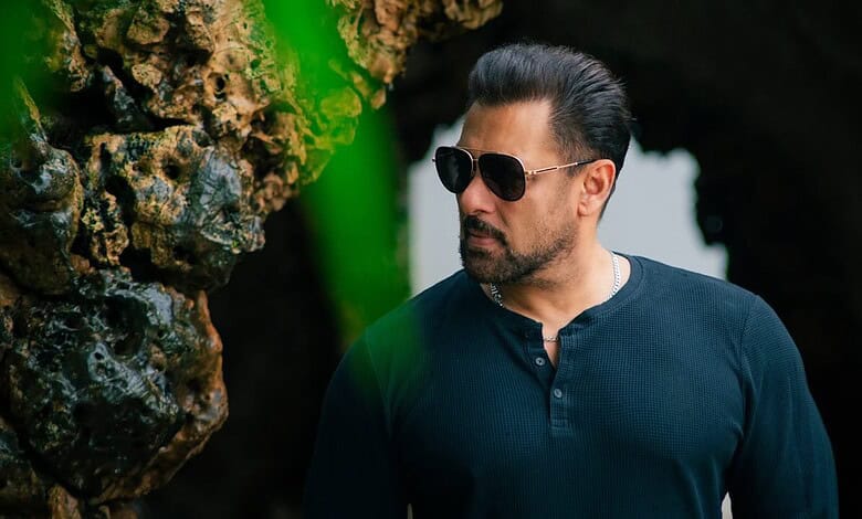 Salman Khan in a casual outfit with sunglasses outdoors near rocks and greenery.