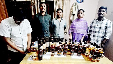Group of five people standing behind a table with numerous bottles of alcohol.