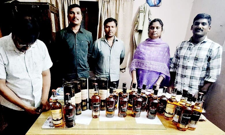 Group of five people standing behind a table with numerous bottles of alcohol.