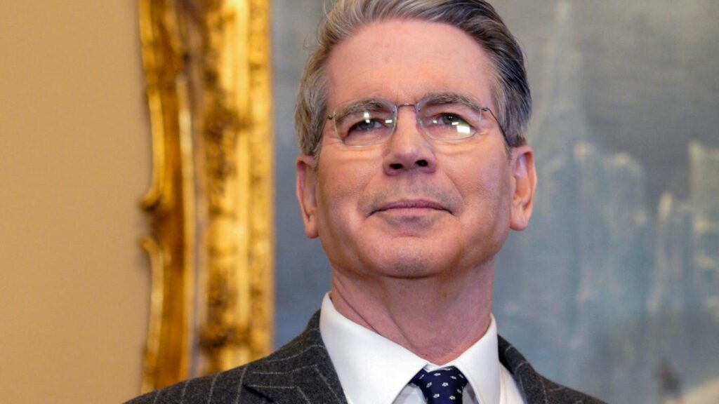 Bessent, a middle-aged man with glasses, in a formal suit, speaking at a diplomatic event.