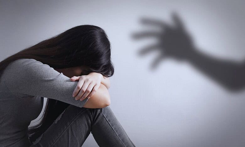 Woman sitting with head down, shadow of a hand reaching towards her on the wall.