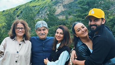 Group of five smiling people outdoors with green hills in the background.
