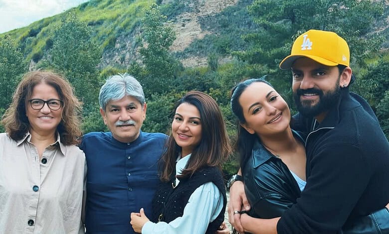 Group of five smiling people outdoors with green hills in the background.