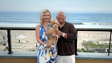 Happy couple with a dog on a balcony overlooking the beach in en_GB.